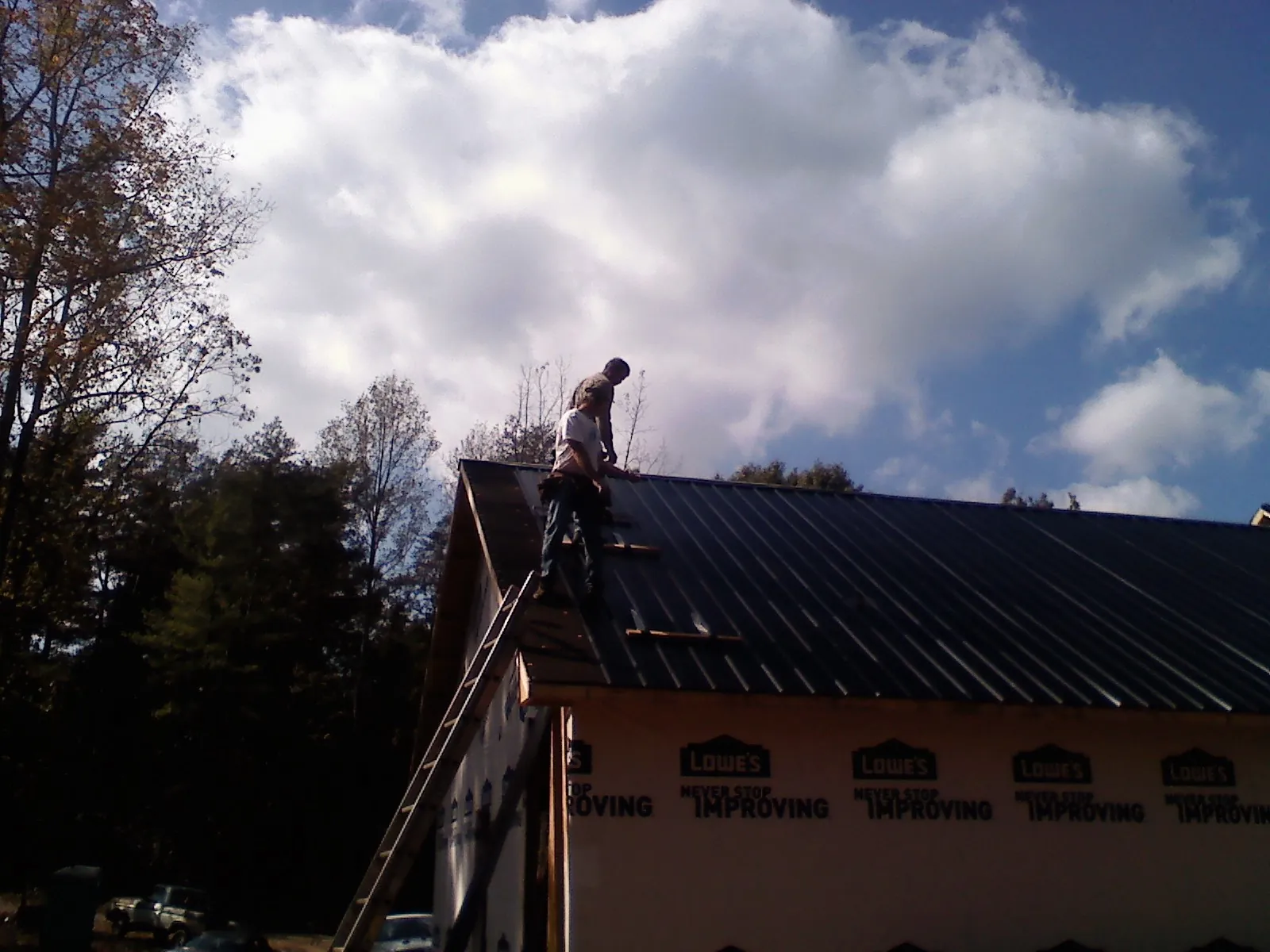 Roofer fastening dark metal panels high against a cloudy sky, from a Roof Inspection job in Rosedale