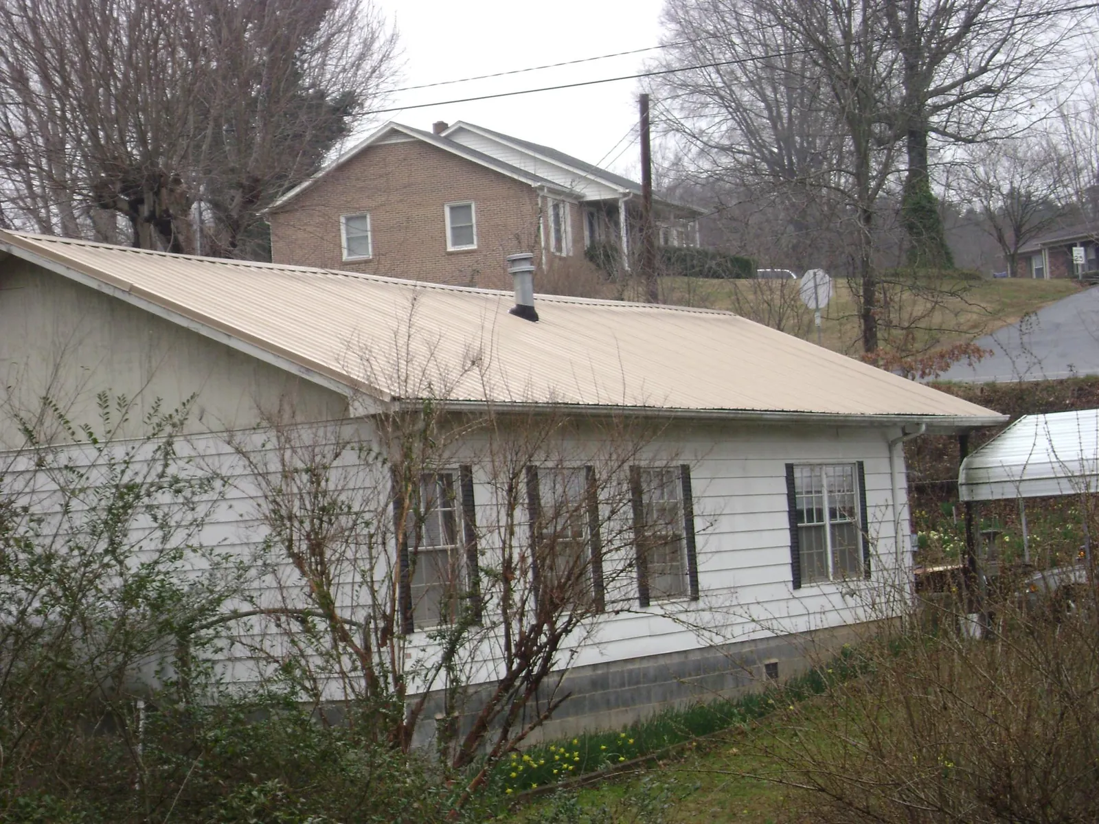 Tan metal roof on a white sided house set into a hillside — Commercial Roofing by Roofing Brothers in Rosedale